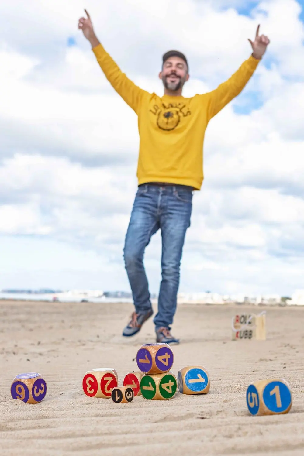 Joueur sautant de joie sur la plage au milieu de Kubbs Roll Kubb colorés et numérotés